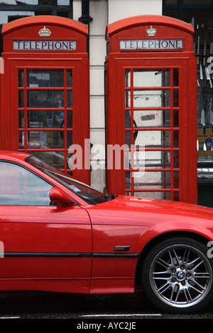 Due dei mitici red London cabine telefoniche con un rosso auto parcheggiate accanto a loro. Foto Stock