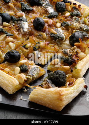 Close up di un pissaladiere pizza con olive nere acciughe e pinoli su nero vassoio da forno Foto Stock