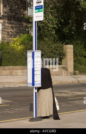 Vista posteriore di una donna in attesa presso la fermata degli autobus per il trasporto pubblico in una giornata di sole in ambiente urbano Dundee,UK Foto Stock