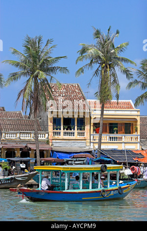 Barche di palme vecchi edifici su Hoi An città storica Thu Bon riverfront metà Vietnam Foto Stock