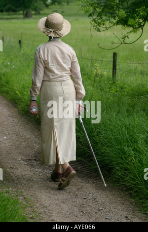 Donna inglese di età degli anni settanta passeggiate nella campagna inglese con bastone Foto Stock