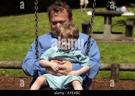 La Newstead Abbey il parco giochi per bambini di età di Lewis su due altalene con il suo papà Foto Stock