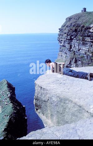 Un turista guardando oltre il bordo mentre che stabilisce le scogliere di Moher Irlanda Foto Stock