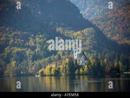 Il lago di Bled XIV-XVII secolo Chiesa sull isola nel lago con i colori autunnali sul fianco della montagna al di là; Slovenia Foto Stock