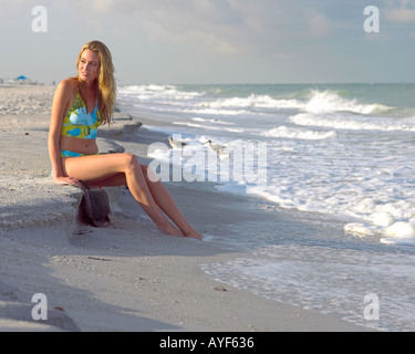 Giovane donna in costume da bagno si siede pacificamente lungo Indian Rocks Beach Florida USA litorale nelle prime ore del mattino Foto Stock