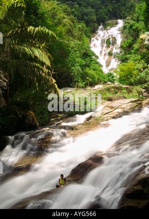 Un ragazzo locale si siede al rapido fluire acqua di Lata Kinjang cascata, Malaysia Foto Stock