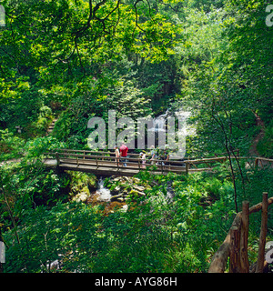 Famiglia a piedi attraverso una stretta piede legno ponte con cascate sotto a Watersmeet su Exmoor North Devon England Foto Stock