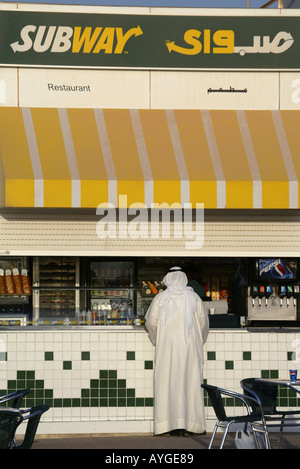 Un uomo Kuwati thaub in abiti tradizionali ordini a una fermata della metropolitana ristorante fast food lungo il molo Sharq a Kuwait City. Foto Stock