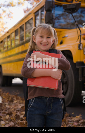 Ragazza abbracciando la scuola prenota nella parte anteriore del bus di scuola Foto Stock