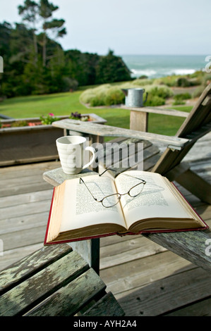 Una serena mattina con un libro e un caffè sul ponte di una casa che si affaccia sul mare Foto Stock