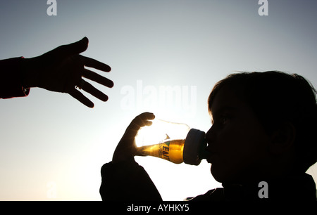 Bambino di bere dalla bottiglia mentre la mano del Padre raggiunge Foto Stock