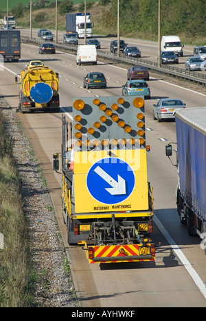 Spazzatrice stradale meccanica e veicolo di protezione con freccia segno spazzare pietre dalla francese drenaggio vista posteriore del traffico guida su M25 autostrada Essex UK Foto Stock