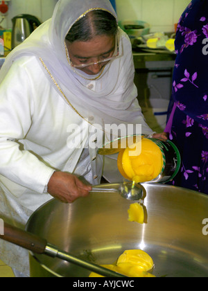 Centro Khalsa Tooting Londra Inghilterra donna la cottura in cucina versando il ghee in una padella il ventesimo anniversario della morte di Guru Tegh Bahadur Foto Stock