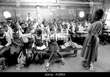 B/N di un insegnante femminile con una classe piena di alunni in una scuola rurale africana. Lesotho Foto Stock