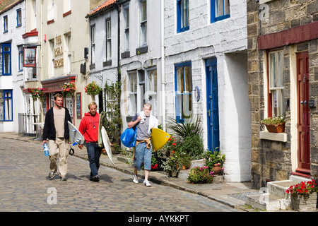 Surfers voce per la spiaggia in High Street in Staithes, North Yorkshire Foto Stock