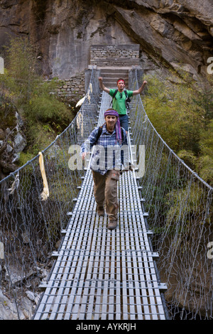 Il trekking attraversare un ponte di sospensione oltre il NAR PHU fiume nell'ANNAPURNA CONSERVATION AREA NEPAL HIMALAYA MR Foto Stock