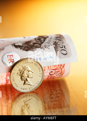 Una moneta in piedi accanto a laminati Pound sterling nota Foto Stock