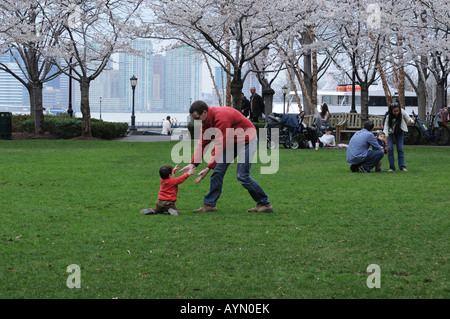 In una bella giornata di primavera in Battery Park City, un padre aiuta il suo figlio che è caduto come si impara a camminare. Foto Stock