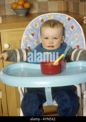 Bambino seduto in un seggiolone rifiutando il suo cibo Foto Stock