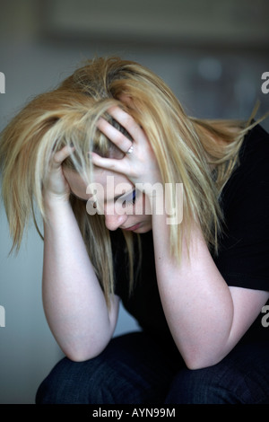 primo piano della testa e spalle di giovane bionda capelli ragazza adolescente seduta con testa nelle sue mani a casa nella sua cucina milleniale fiocco di neve Foto Stock