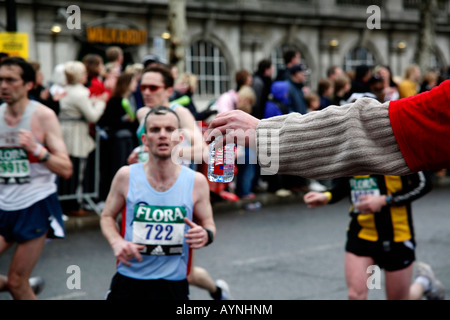 Una mano che offre acqua in bottiglia per i corridori nella maratona di Londra. Foto Stock