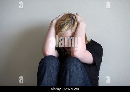 Giovani dai capelli biondi teenage donna seduta tenendo la testa nelle sue mani con la schiena contro una parete Foto Stock