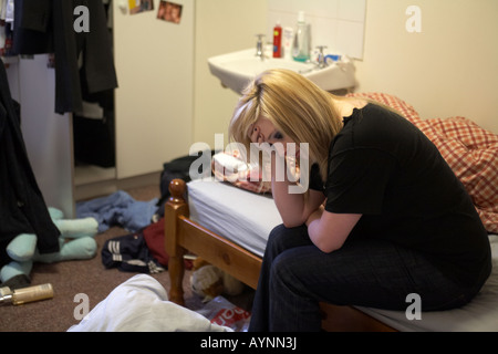 Adolescente giovane donna seduta sul letto in disordine hmo monolocale matrimoniale tenendo la testa in una mano Foto Stock