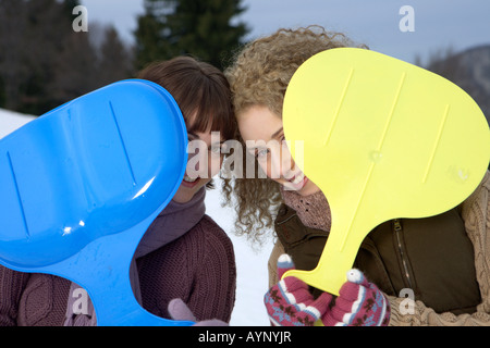 Two young women holding plastic slide-shovels in their gloved hands, portrait Foto Stock