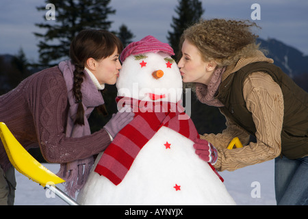 Due giovani donne baciare un pupazzo di neve Foto Stock
