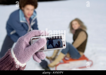 Persona di scattare una foto di una coppia eterosessuale nella neve con un telefono cellulare, il fuoco selettivo Foto Stock