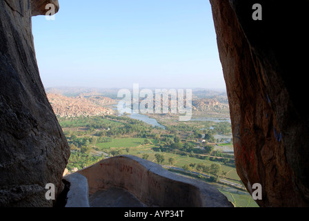 Vista attraverso giganteschi massi sulla collina Anjaneya giù per il lussureggiante paesaggio di Hampi con il fiume Tungabhadra che fluisce attraverso di esso Foto Stock