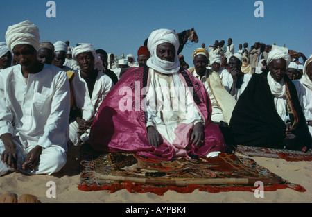 Il Ciad Centrafrica religione islam musulmani chief seduta sul suolo alla preghiera durante il festival circondato dalla folla di persone gruppo Foto Stock