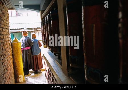 Coppia di tibetani anziani in piedi vicino a una fila di ruote di preghiera buddiste a Dharamsala, in India. Foto Stock