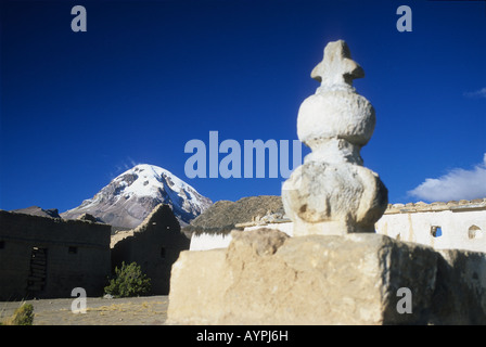 Cairn con croce di pietra in Tomarapi village square e Sajama vulcano, Sajama Parco Nazionale, Bolivia Foto Stock