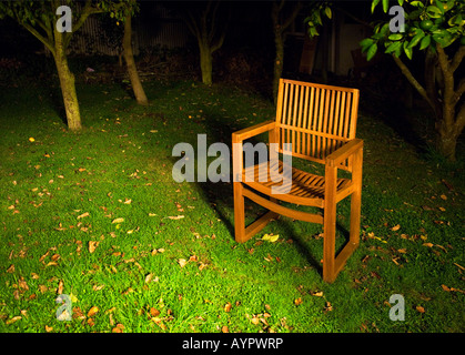 Sedia in legno nel giardino di notte, su di un prato con alberi in background. Foto Stock