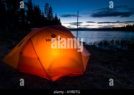 Tenda illuminato dall'interno al tramonto su un lago, Femundsmark, Norvegia Foto Stock