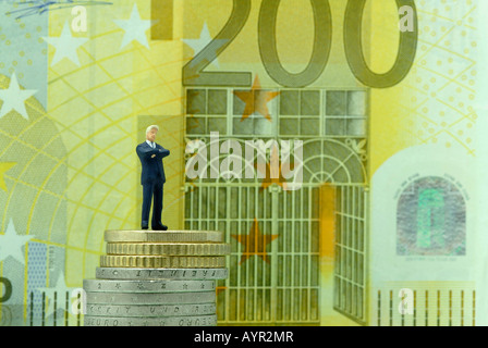 Soddisfatto-cercando imprenditore in piedi su una pila di monete di fronte a 200-Euro bill Foto Stock