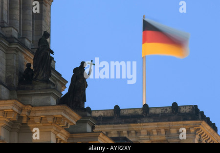 Bandiera tedesca sventolare sul tetto del Reichstag e una statua che tiene una croce (simbolo per la chiesa cristiana), Berlino, Germania Foto Stock