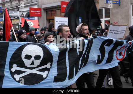 Dimostrazione contro la guerra a Poznan, Polonia. I manifestanti tengono uno striscione con teschio e ossa incrociate e bandiere anarchiche durante una protesta di strada. Foto Stock