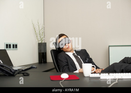 Imprenditore indossando maschera dorme seduto alla scrivania Foto Stock