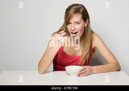 Giovane donna mangiare cereali a un tavolo per la colazione Foto Stock