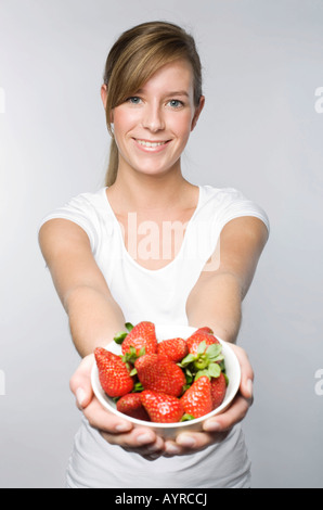 Sorridente giovane donna con lunghi biondo scuro capelli offrendo una tazza di fragole fresche Foto Stock