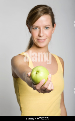 Sorridente giovane donna che offre una mela verde Foto Stock