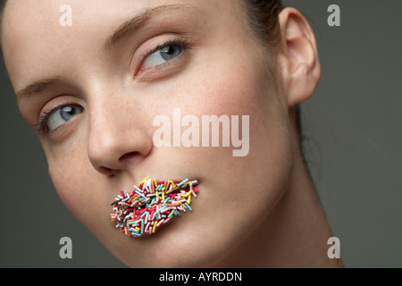 Giovane donna con granuli multicolore sulle labbra, close-up Foto Stock