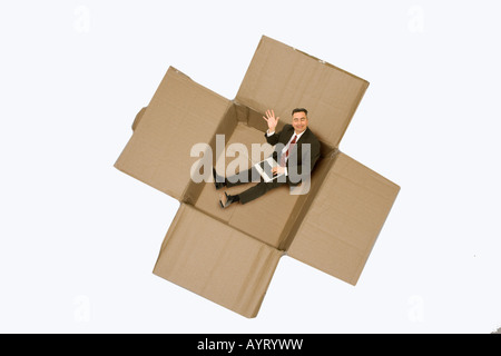 Imprenditore con un notebook seduto in una scatola di cartone Foto Stock