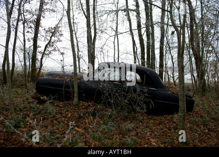 Lato in vista della vecchia derelitti nero auto d'epoca che giace dimenticato in un bosco invernale Foto Stock