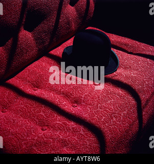 Black Bowler cappello sul divano rosso Foto Stock