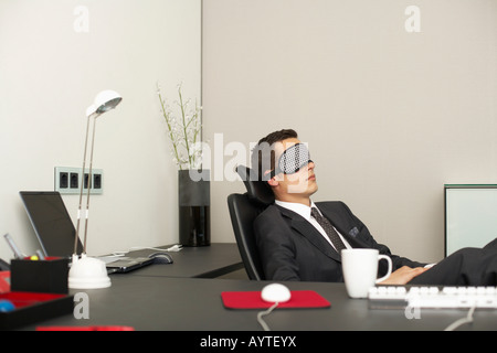 Imprenditore indossando maschera dorme seduto alla scrivania Foto Stock