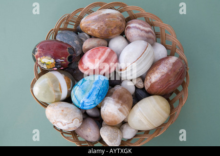 Ancora la vita di studio vicino di un cesto in vimini tenendo una selezione di pietre levigate e decorativi in pietra di uova Foto Stock