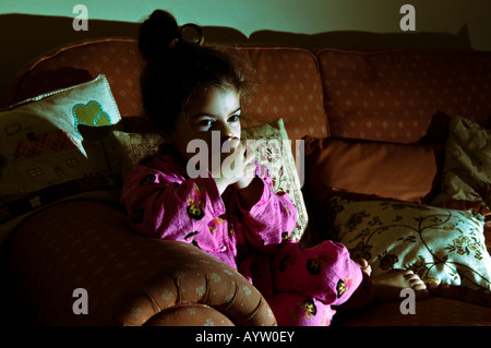 Una giovane ragazza orologi a tarda notte solo televisivo su un lettino illuminato dalla luce della televisione Foto Stock